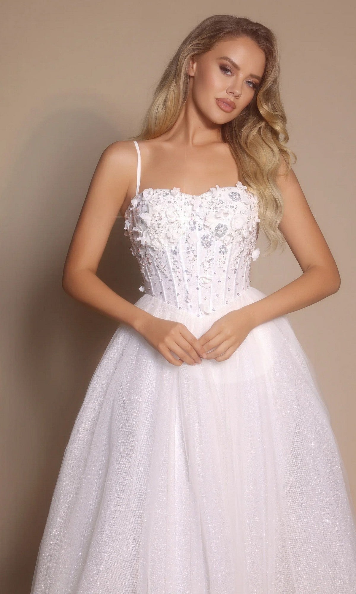 A woman poses elegantly in the Portia and Scarlett PS26146 Glitter Prom Ball Gown, featuring white glitter tulle, a boned-corset bodice with thin straps, and a full skirt against a neutral background.